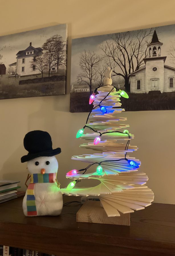 Handmade wooden spiral tree decorated with a string of colorful holiday lights, next to a plush snowman
